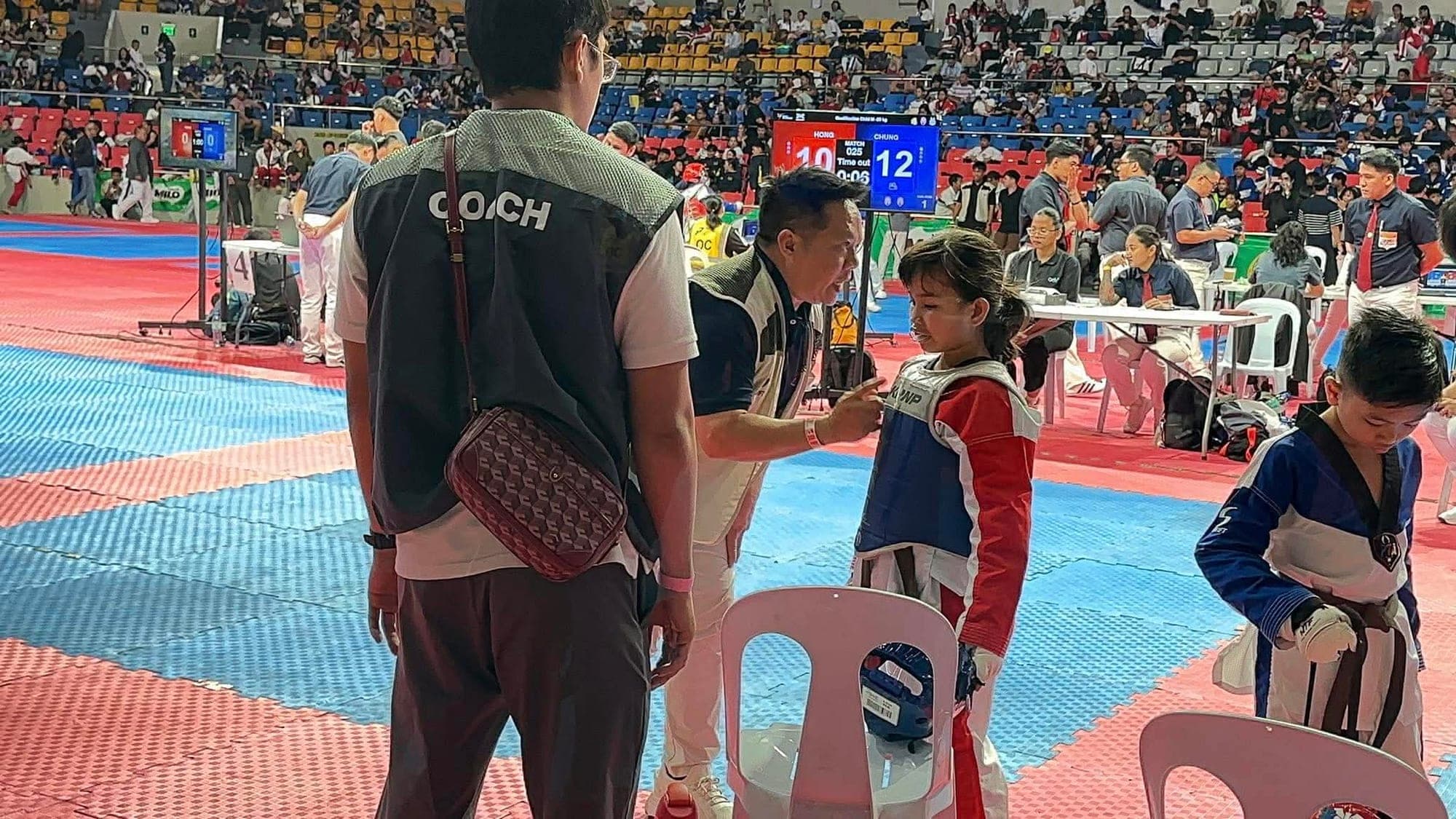 A WVT coach giving advice to a young athlete in a chest protector during a break between rounds.