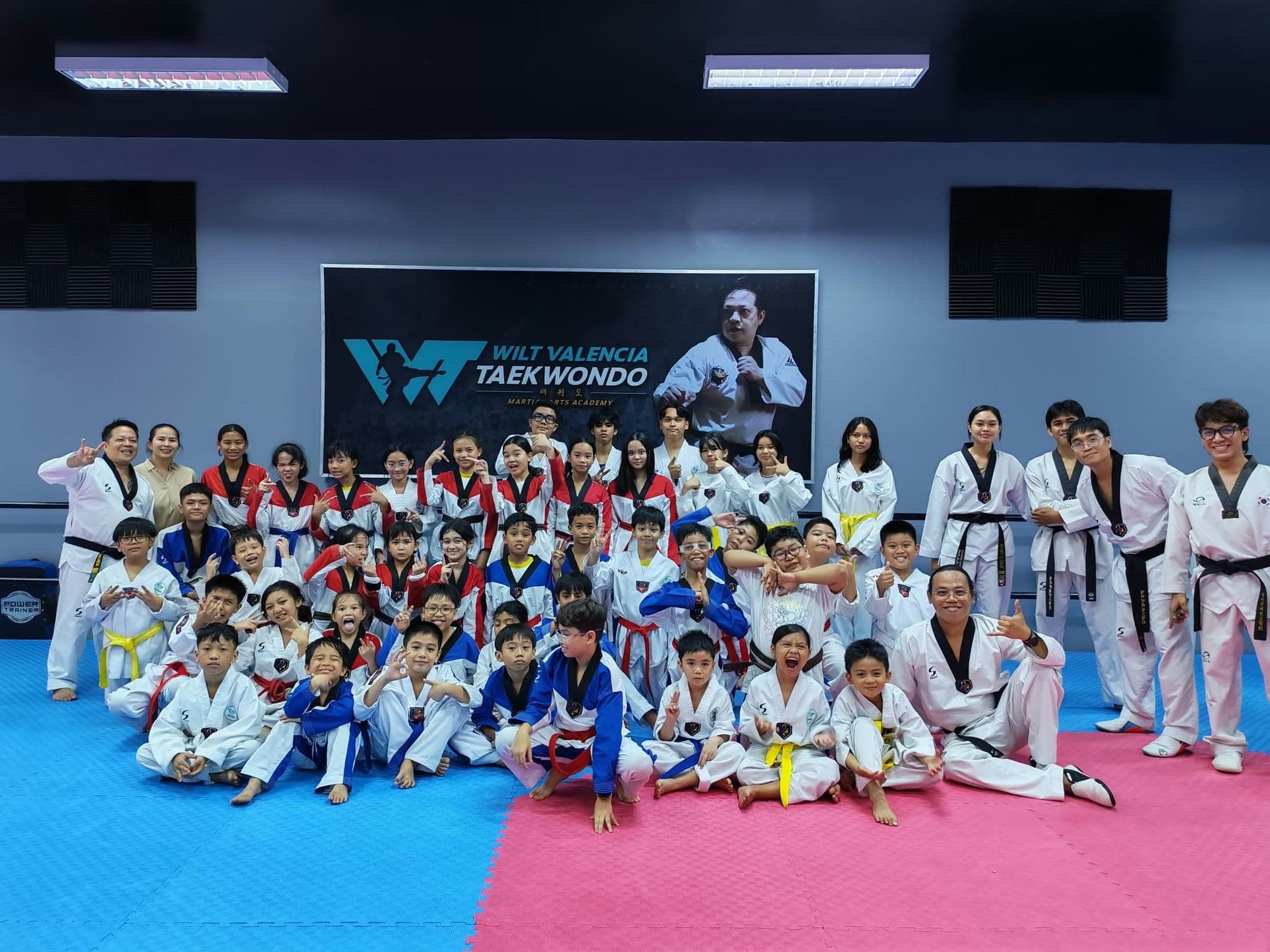 A large group of WVT students of all ages and belt colors posing together on the mat at the academy.
